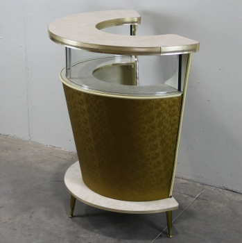 Formica, cristal, madera, latón y aluminio. Tapizado en vinilo dorado.
Tiene un abrebotellas incorporado.